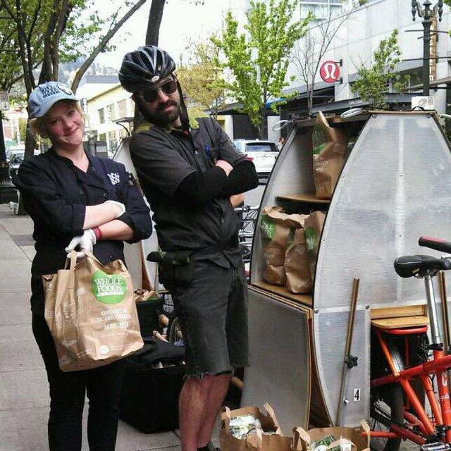 Whole foods catering employee and Portland Pedal Power delivery person loading up bike with food